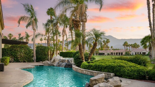 Ein Pool mit Wasserfall, umgeben von Palmen und Blick auf einen Golfplatz.