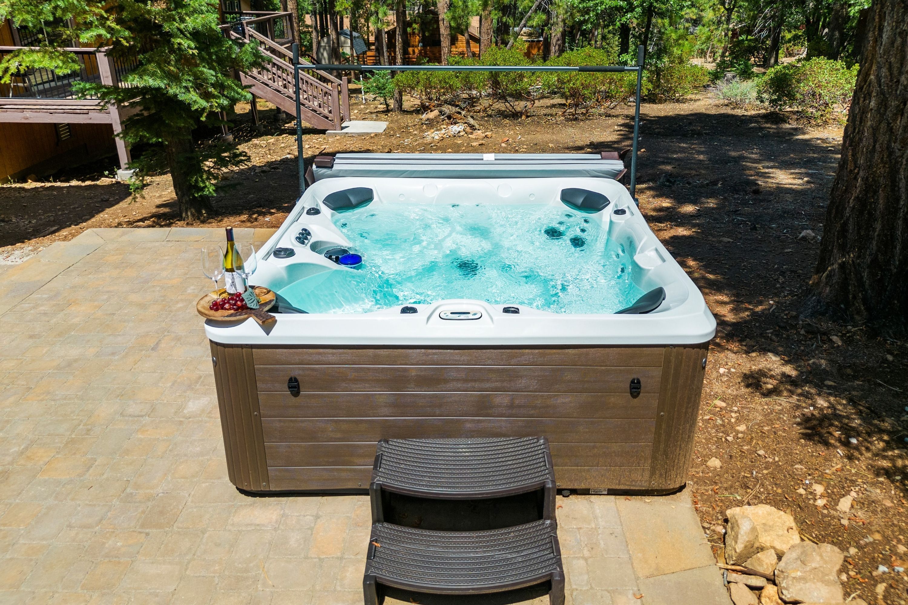A hot tub with a wooden exterior, a seating area, and a poolside setting with trees and a wooden deck in the background.