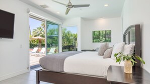 A modern bedroom with a large bed, a ceiling fan, and a view of the outdoors.