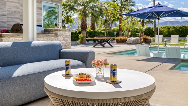 A poolside area with a round table, a sofa, and a patio umbrella.