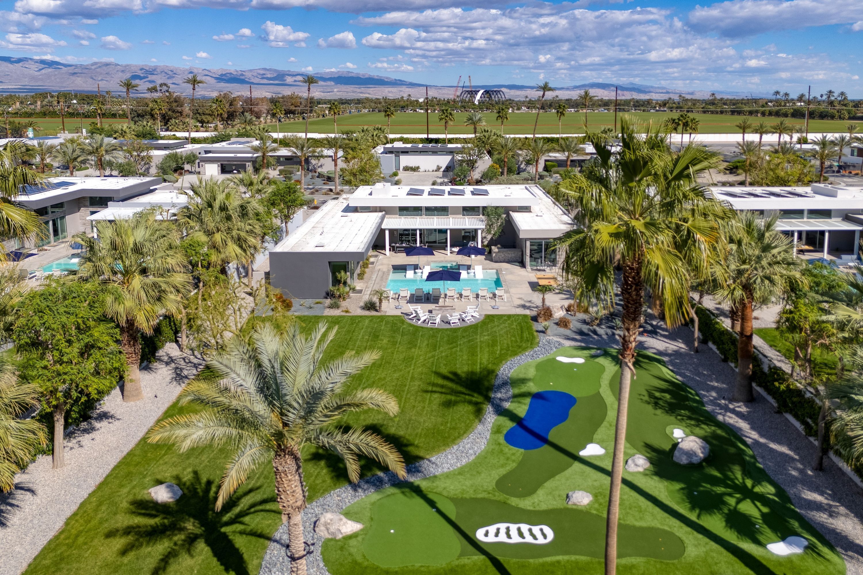 A modern resort with a pool, palm trees, and a golf course.