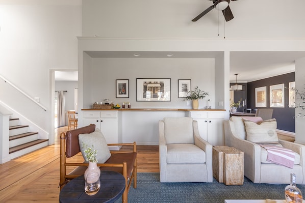A spacious living room with a wooden staircase, a kitchen area with a wooden countertop, and a seating area with two sofas and a coffee table.