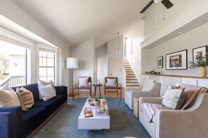 A living room with a dark blue sofa, beige armchairs, a white coffee table with snacks, and a staircase leading to an upper level.