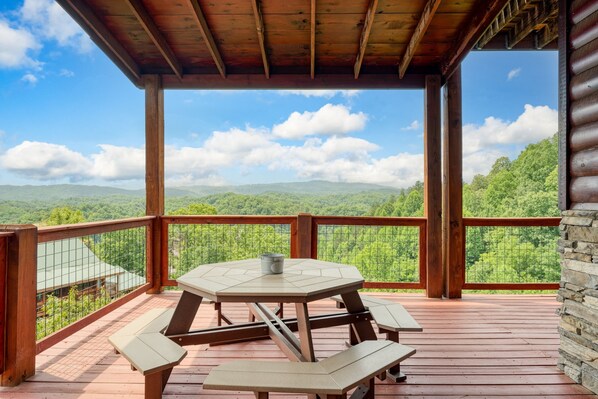 A wooden deck with a table and benches, overlooking a mountainous landscape.