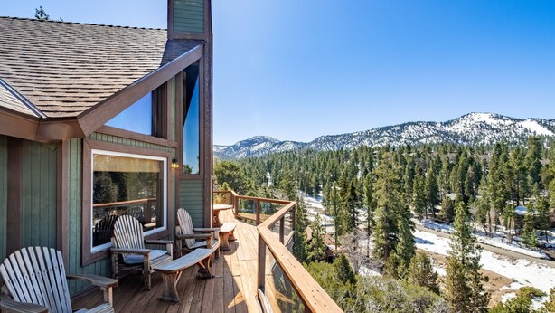 A wooden deck with Adirondack chairs and a table, overlooking a snowy mountain range and dense forest. - Endless View Lodge by Avantstay Incredible Views Close To Bear Mountain Ski Resort w Hot Tub (Big Bear Lake)