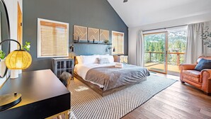 A modern bedroom with a large bed, a desk, a chair, a ceiling fan, and a balcony with a view of trees. - Endless View Lodge by Avantstay Incredible Views Close To Bear Mountain Ski Resort w Hot Tub (Big Bear Lake)