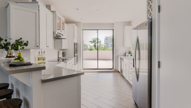 A modern kitchen with white cabinets, a large island, and a sliding glass door leading to an outdoor balcony. - Ivory II By Avantstay Gorgeous Spacious Home w Views Close To Old Town (Scottsdale)