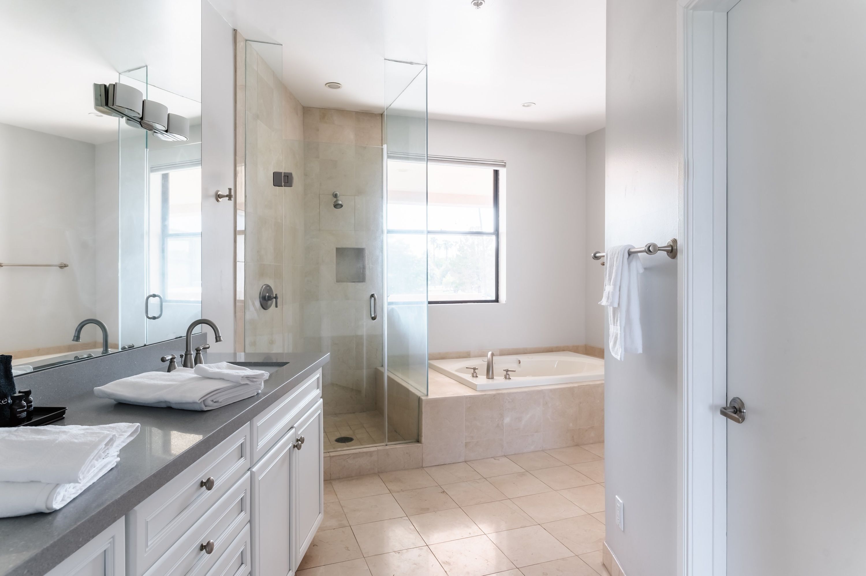 A modern bathroom with a glass-enclosed shower, a large bathtub, and a vanity with a mirror and sink.