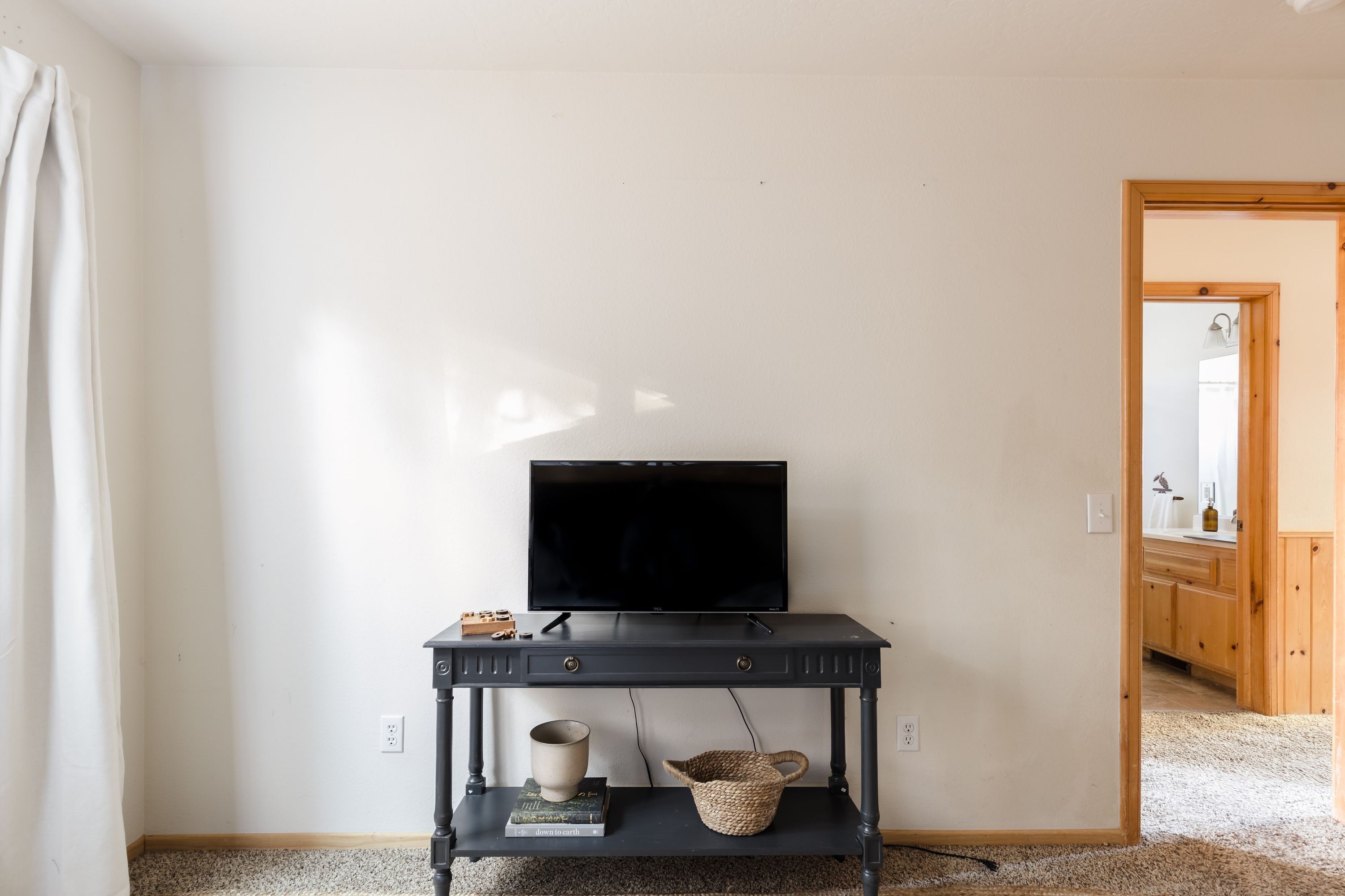 A room with a black TV on a stand, a small shelf with books and a basket, and a door leading to a bathroom.