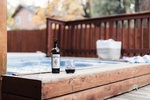 A wooden deck with a hot tub, a bottle of Coppola wine, and a glass. - Jumper By Avantstay Serene Stylish Cabin w Hot Tub (Big Bear Lake)