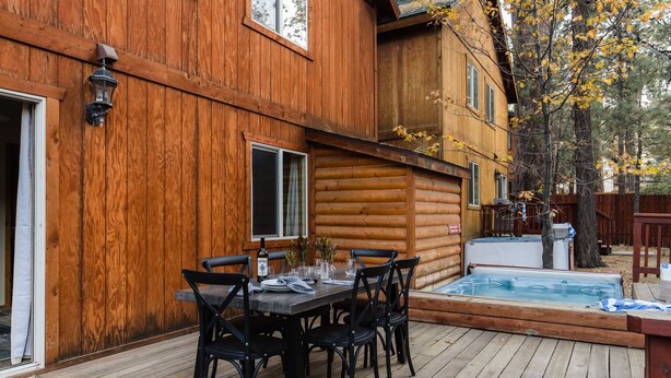 A wooden cabin with a deck, a hot tub, and a dining area with chairs and a table. - Jumper By Avantstay Serene Stylish Cabin w Hot Tub (Big Bear Lake)