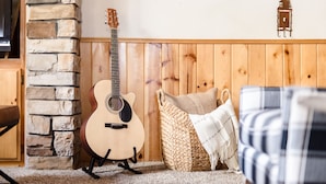 A cozy room with a stone wall, a wooden bench, a woven basket, and a guitar. - Jumper By Avantstay Serene Stylish Cabin w Hot Tub (Big Bear Lake)