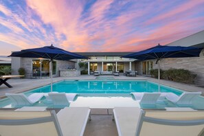 A swimming pool with lounge chairs and umbrellas, surrounded by a modern house with a stone facade and large windows. - Polo Villa 10 by Avantstay Backyard Oasis w Putting Green 260320 6 Bedrooms (La Quinta)