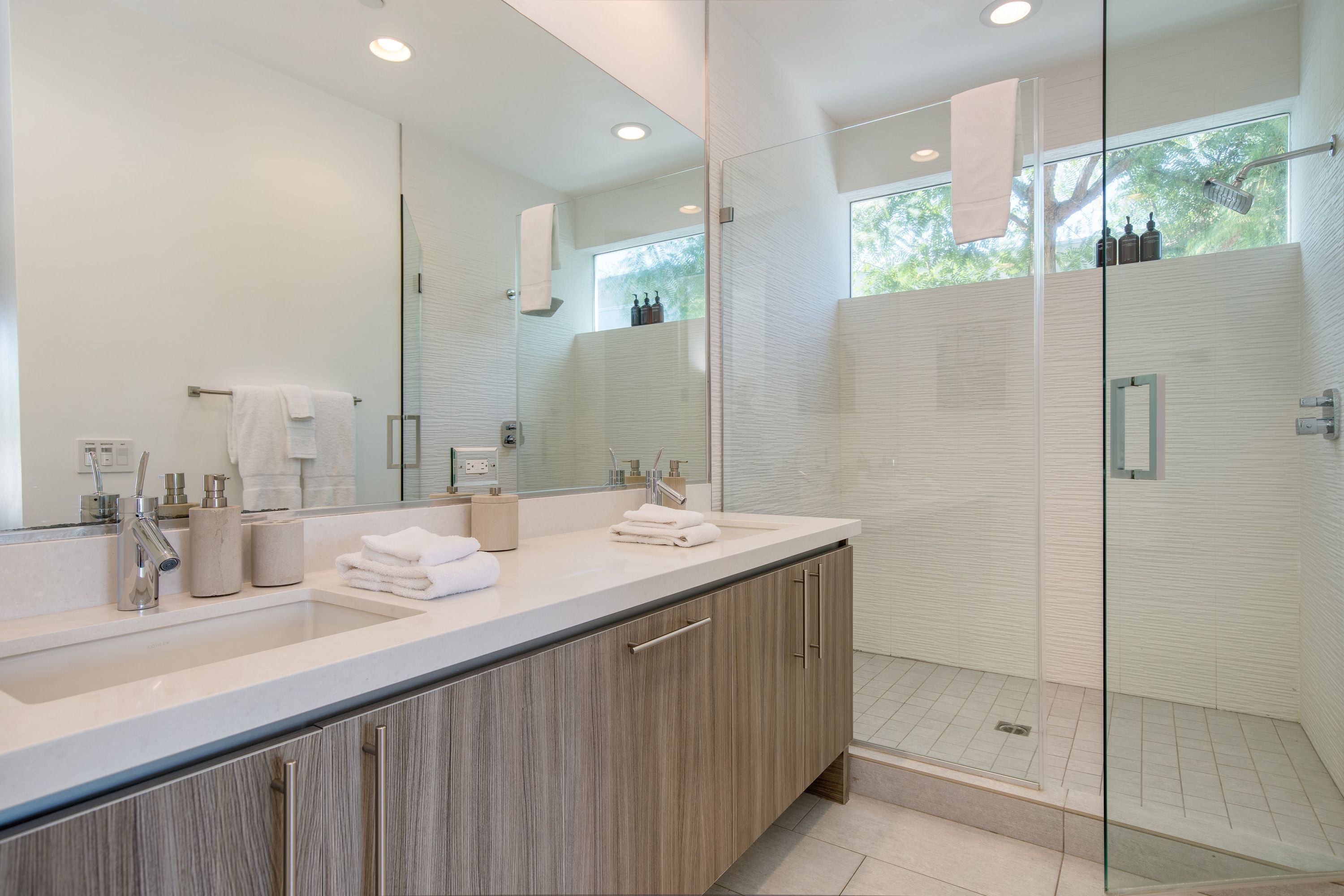 A modern bathroom with a large mirror, dual sinks, and a glass-enclosed shower area.