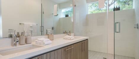 A modern bathroom with a large mirror, dual sinks, and a glass-enclosed shower area.