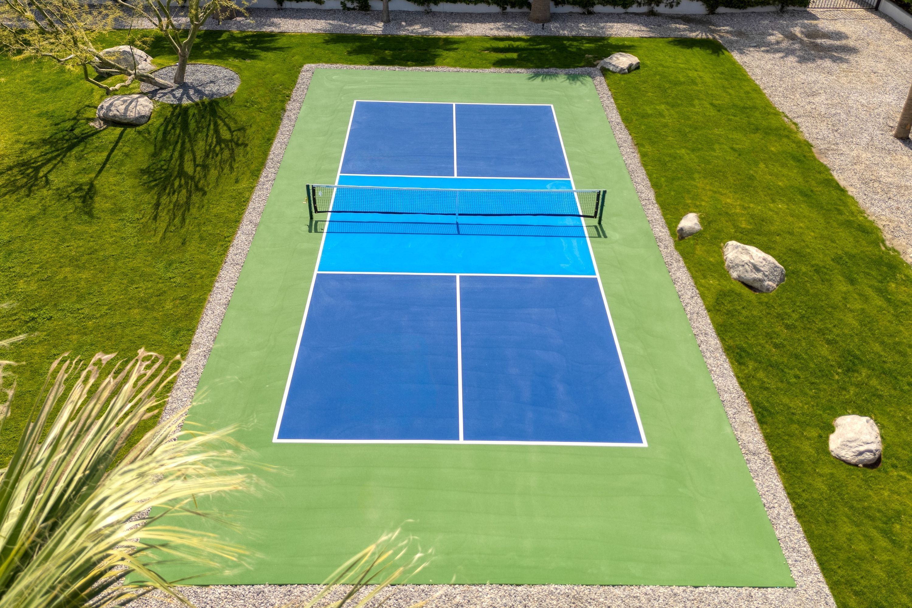 A tennis court with a net, surrounded by a well-maintained grassy area and decorative rocks.