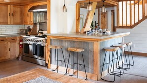 Une cuisine avec des meubles en bois, une cuisinière en acier inoxydable et des tabourets de bar.