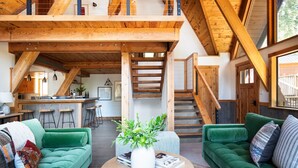 Un vaste espace de vie comprenant deux canapés verts, une table basse et un escalier menant à un niveau supérieur.