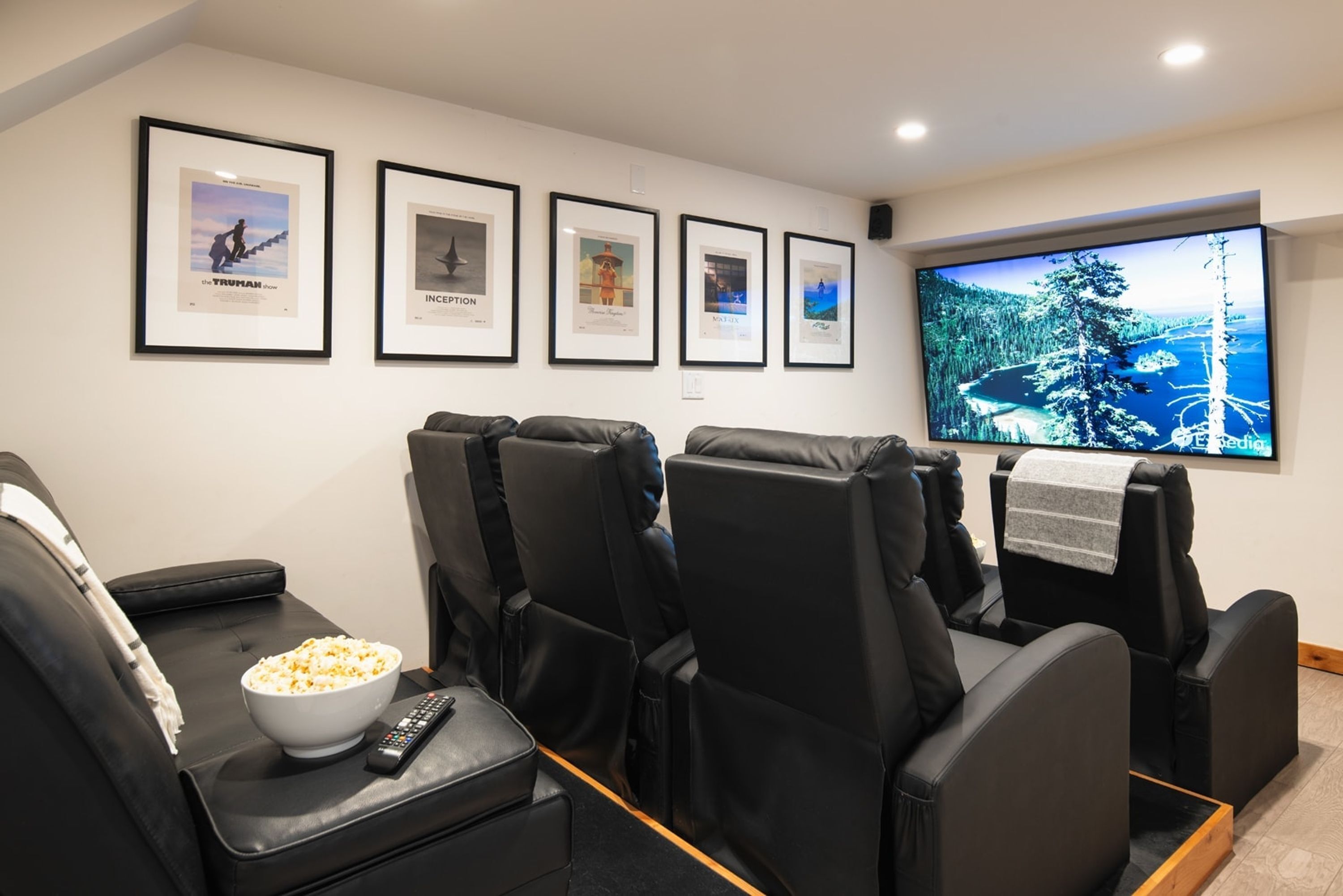 A home theater with black leather recliner seats, a large flat-screen TV, and framed movie posters on the wall.