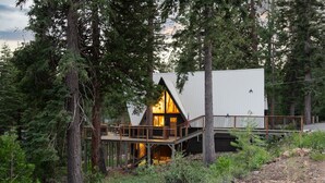 Une cabane dotée d’une terrasse en bois et d’une grande fenêtre, entourée d’une forêt dense.