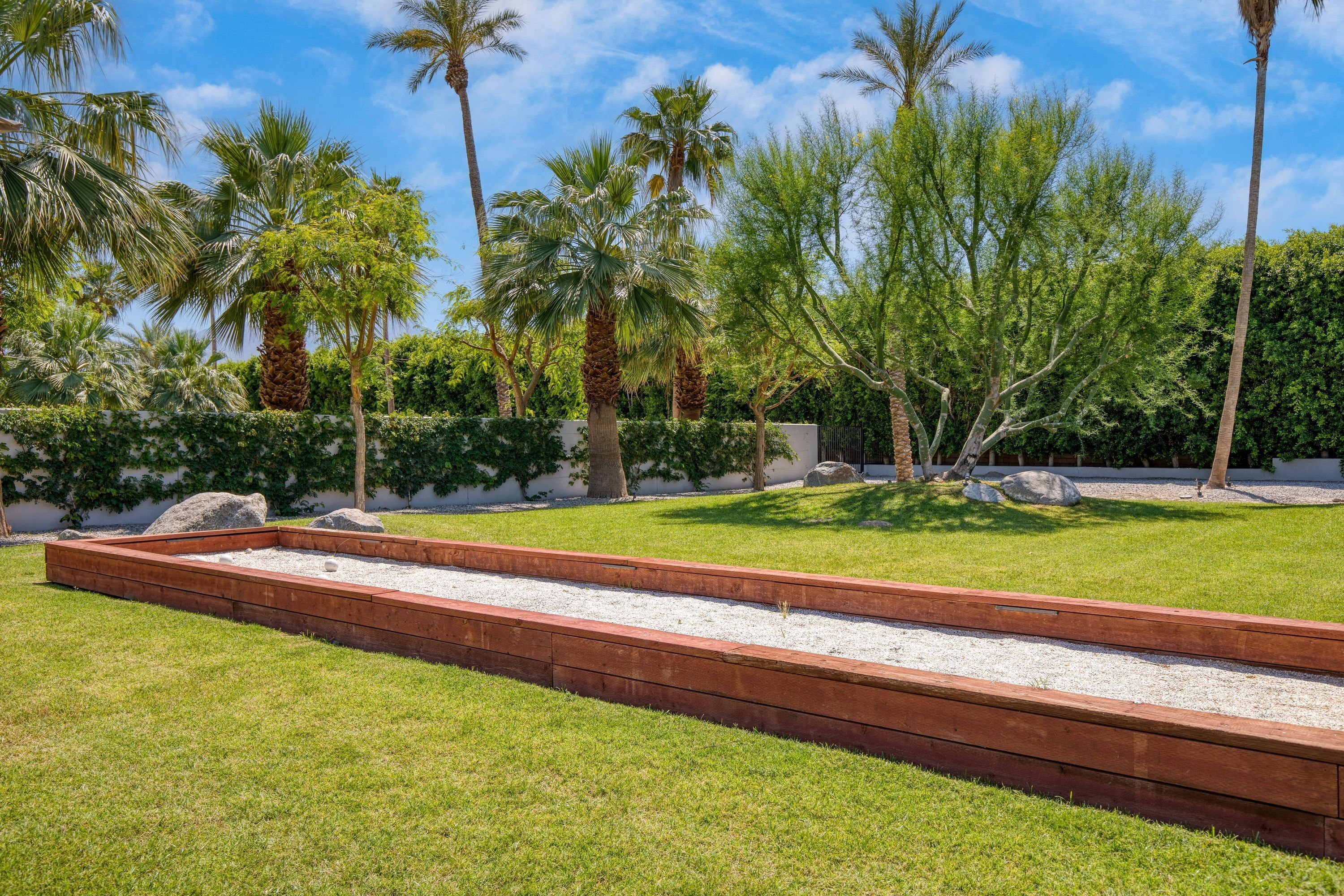 A landscaped garden with palm trees, a wooden deck, and a well-maintained lawn.