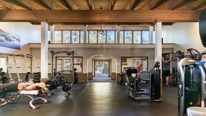 Ein Fitnessstudio mit diversen Trainingsgeräten, einem zentralen Weg und großen Fenstern, die viel Tageslicht hereinlassen.