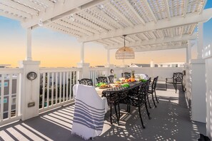 Una terrazza esterna con una pergola bianca, un tavolo da pranzo apparecchiato con sedie e una lampada decorativa sospesa.