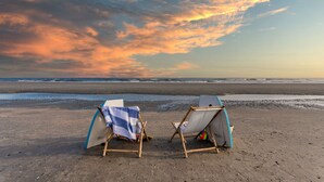 Two beach chairs with surfboards on a sandy beach with a view of the ocean and a sunset sky. - Sand Dune Sea Shell by Avantstay Gorgeous 2 Home Rental w 12 BRs (Isle of Palms)