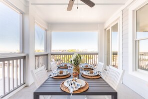 A covered outdoor dining area with a table set for four, surrounded by white railings and large windows. - Sand Dune Sea Shell by Avantstay Gorgeous 2 Home Rental w 12 BRs (Isle of Palms)