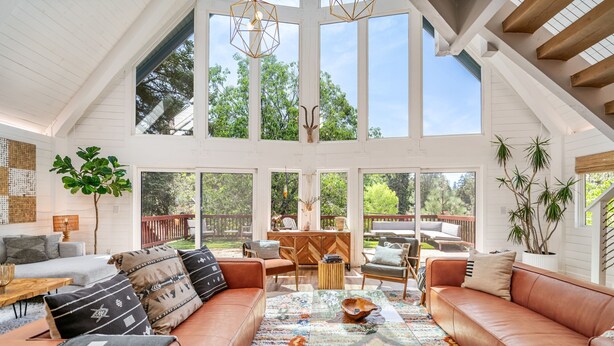A spacious living room with a large brown leather sofa, a colorful rug, and a dining area with wooden furniture.