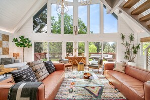 A spacious living room with a large brown leather sofa, a colorful rug, and a dining area with wooden furniture. - Oak and Luna by Avantstay Beautiful Big Bear Home w Hot Tub Home Theatre Ping Pong (Big Bear Lake)