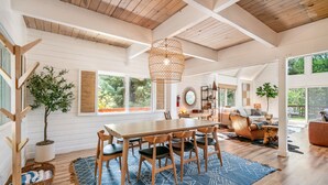 A spacious dining area with a wooden table and chairs, a hanging light fixture, and a view of the outdoors.