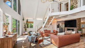 A spacious living area with a large sofa, a wooden coffee table, and a TV. There is a staircase leading to an upper level with a balcony.