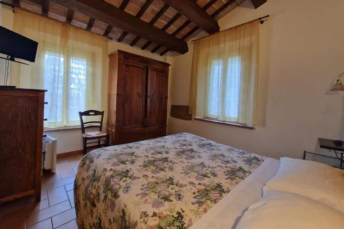 A bedroom with a bed, wooden wardrobe, chair, and a desk with a lamp.