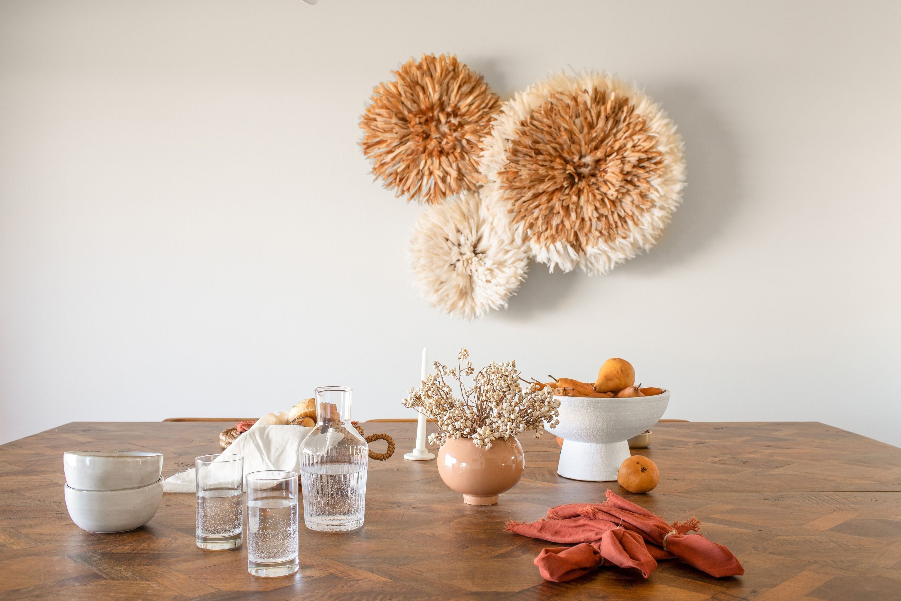 A wooden table with a white vase, a bowl of fruits, and a bottle of water.