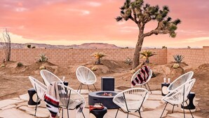 Un paysage désertique avec un foyer, des chaises blanches et un grand arbre.