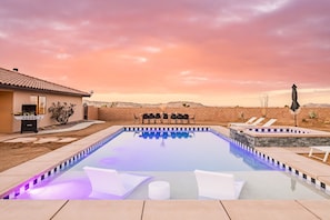 A swimming pool with lounge chairs and a barbecue area, surrounded by a brick wall and desert landscape.