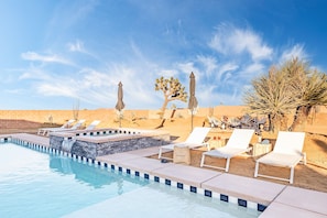 A pool area with lounge chairs, a small waterfall feature, and desert plants.