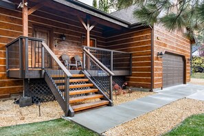 A log cabin with a wooden exterior, a front porch with two chairs, a staircase, and a garage.