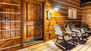 A wooden cabin with a wooden door, a welcome sign, a lantern, and a deck with chairs. - Lazy Bear Lodge by Avantstay Pine Tree Paradise w Game Room (Big Bear Lake)