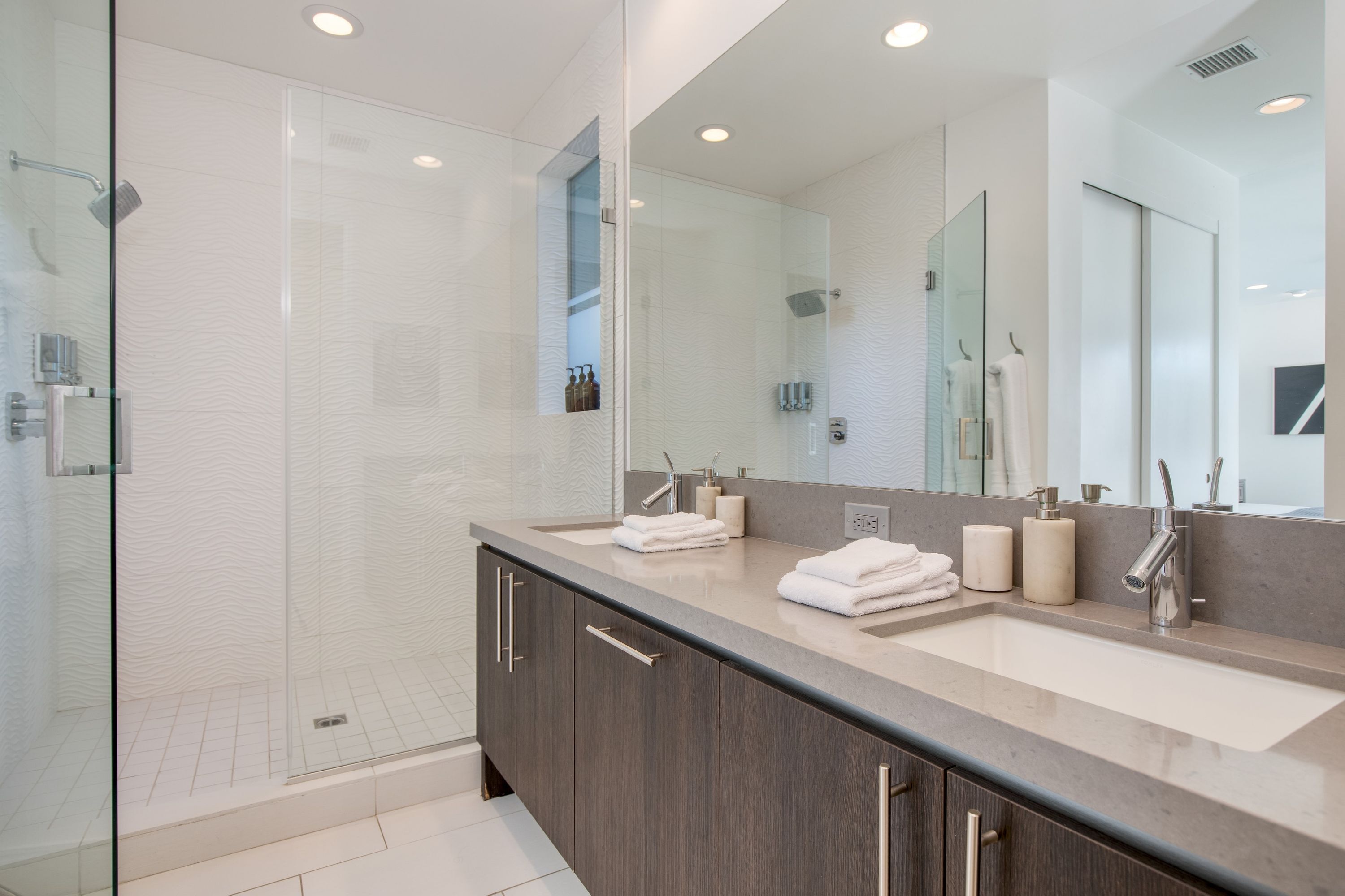 A modern bathroom with a glass-enclosed shower, a large vanity with dual sinks, and a large mirror.