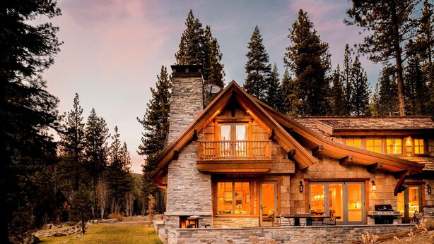 A log cabin with a stone chimney, large windows, and a balcony.