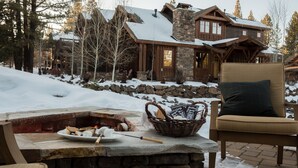 A stone fireplace with a plate of food, a basket, and a chair outside a lodge with a stone facade and wooden exterior. - Maple by Avantstay Modern Mountain Home w Cozy Fire Pit 15 Mins frm Northstar (Truckee)