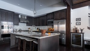 A modern kitchen with dark wood cabinets, stainless steel appliances, a large island with stools, and a unique backsplash. - Maple by Avantstay Modern Mountain Home w Cozy Fire Pit 15 Mins frm Northstar (Truckee)