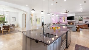 Una cocina moderna con una isla central, un comedor con mesa y sillas, y una sala de estar con sofá y chimenea.