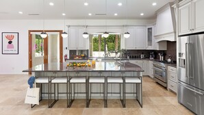 Una cocina moderna con una isla grande, electrodomésticos de acero inoxidable e iluminación colgante.
