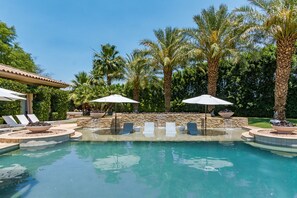 Un área de piscina con sillones de descanso, sombrillas y palmeras.