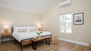 Ein Schlafzimmer mit Bett, Nachttischlampen, einem Nachttisch, einem Fenster und einer Klimaanlage.