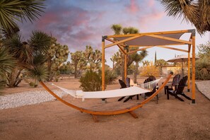 A hammock under a wooden pergola in a desert garden with chairs and a table. - Chuckwalla by Avantstay Joshua Tree Haven w Hot Tub Modern Interior (Yucca Valley)