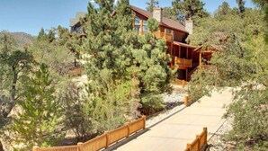 A wooden cabin with a stone chimney, surrounded by pine trees and a wooden deck. - Starlight Retreat by Avantstay Gorgeous Log Style Home w Incredible Views (Big Bear Lake)